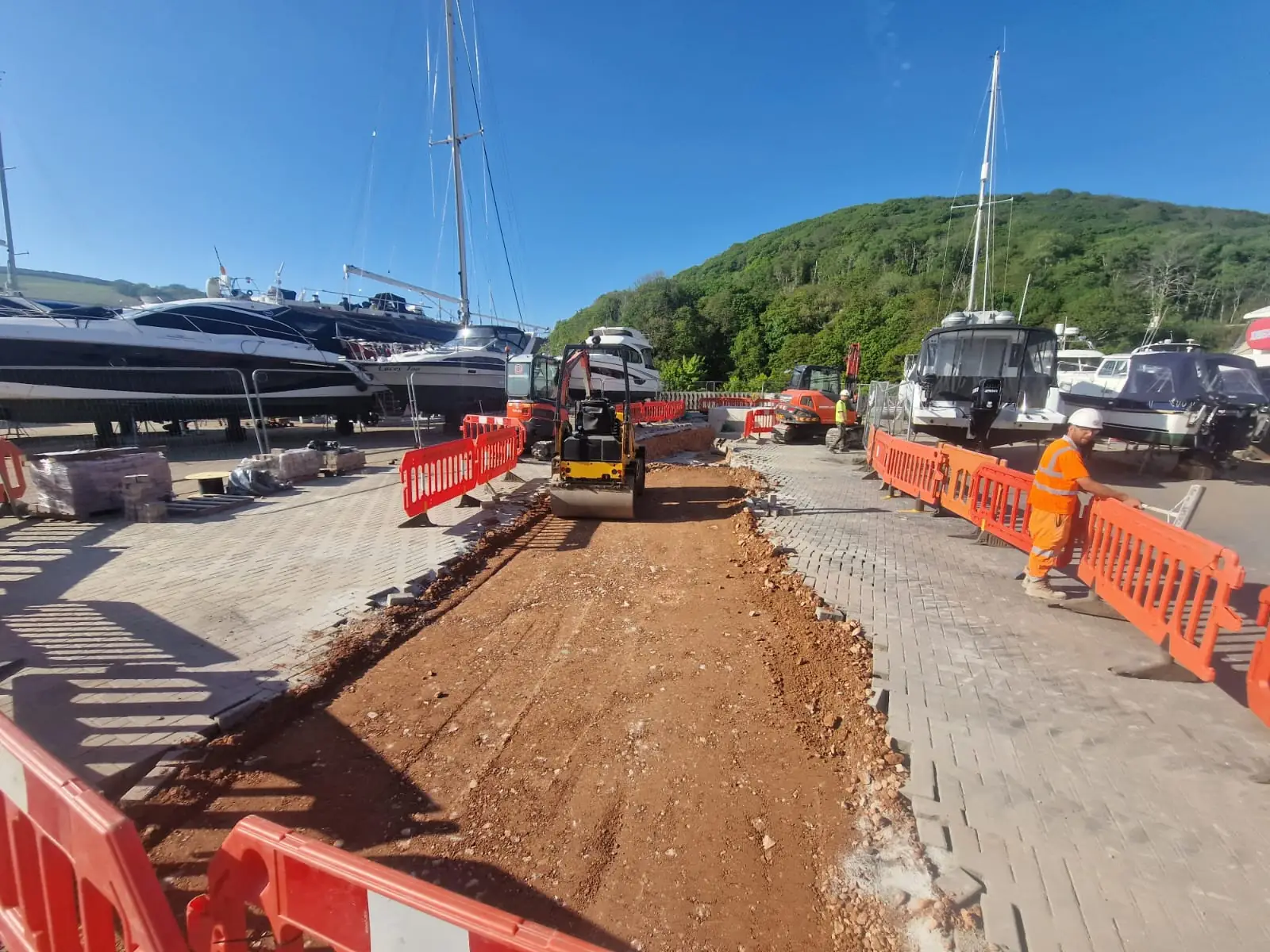 Roller compacting backfill between paving on a marina site