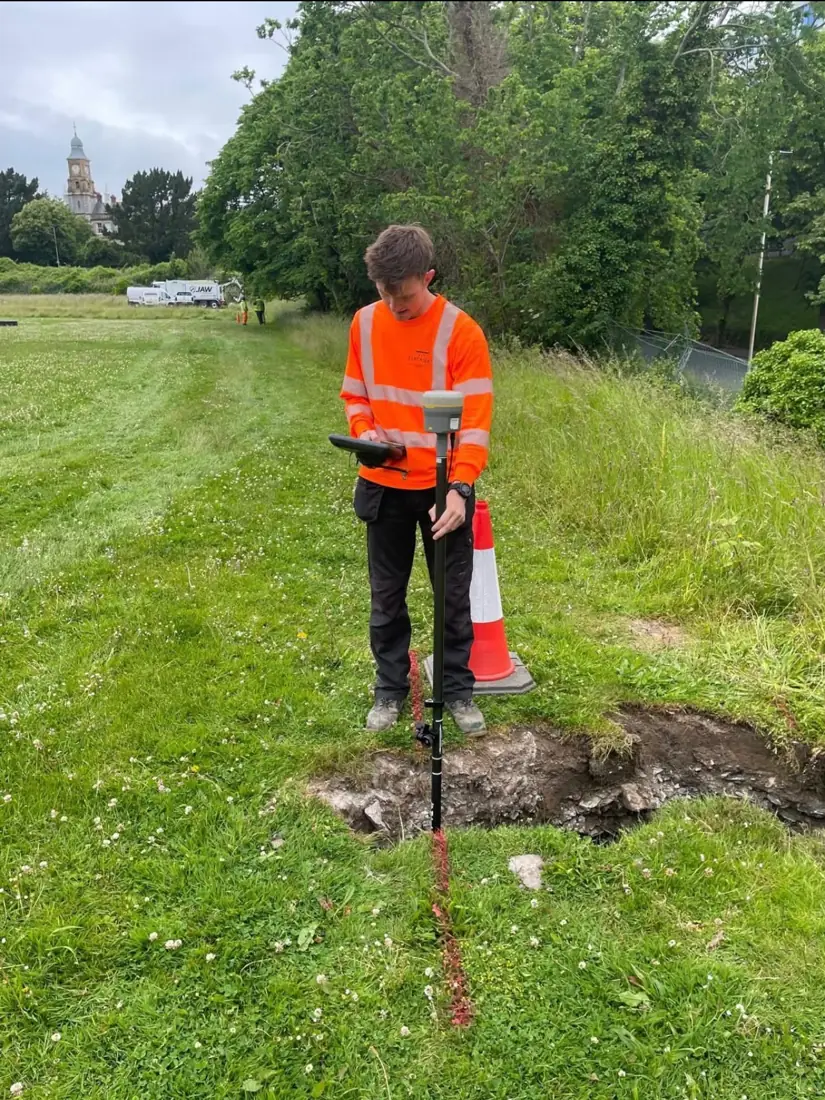 Surveyor recording a trial hole while the vacuum excavator works further along the route